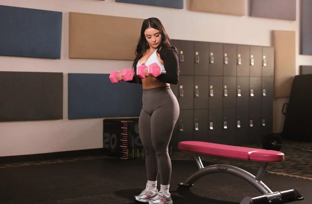 Leslie curling pink dumbbells in a gym in El Paso