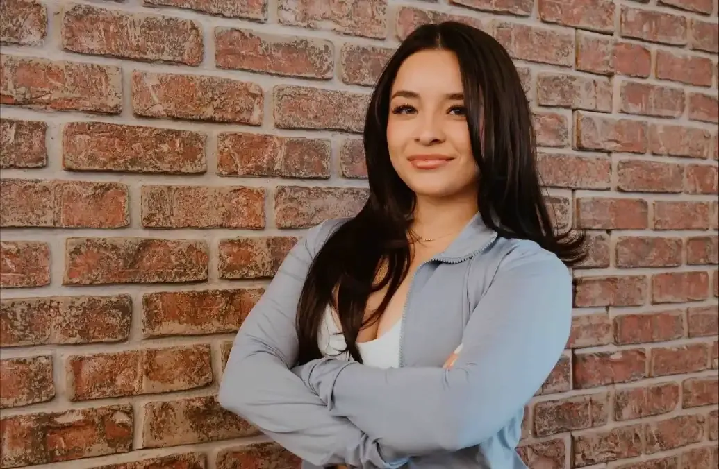Leslie smiling with arms crossed in front of a brick wall